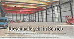 Screenshot eines Zeitungsartikels mit dem Titel "Riesenhalle geht in Betrieb" und der Abbildung einer großen, leeren Lagerhalle